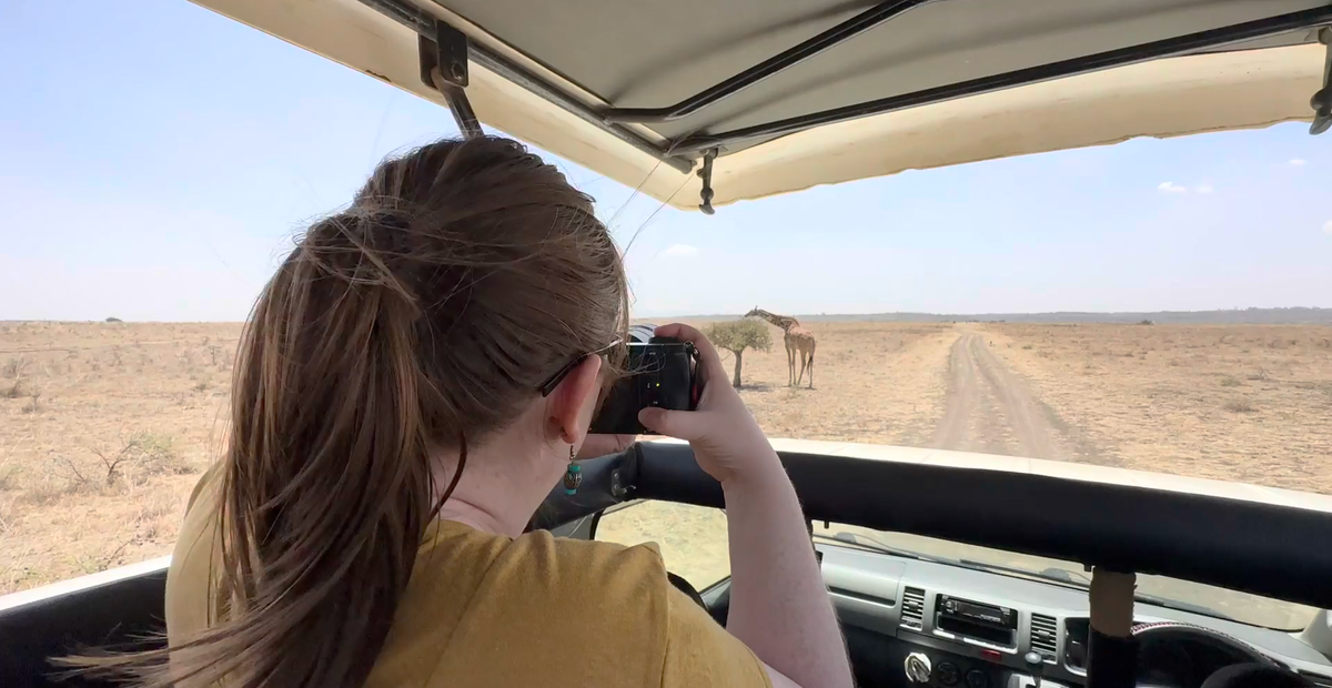 Image of a woman recording footage of a giraffe in Kenya.